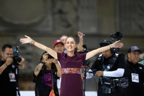 Reuters Mexican presidential candidate Claudia Sheinbaum stands with her arms outstretched on stage at a campaign event. 