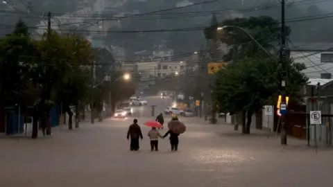 Reuters People walk in a flooded area in the Cavalhada neighbourhood after heavy rains in Porto Alegre, Brazil May 23, 2024.