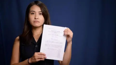 Anthony WALLACE / AFP In this picture taken on August 4, 2020, pro-democracy activist Gwyneth Ho, who was recently banned from standing in upcoming local elections, poses with her disqualification notice at her office in Hong Kong