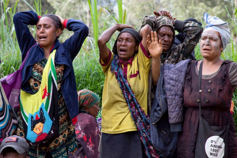 Distraught women watch rescue efforts at the site of a massive landslide in PNG. They their hands on their heads. One has closed her eyes.