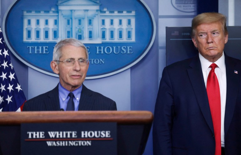 Donald Trump stands next to the White House podium where Anthony Fauci speaks.