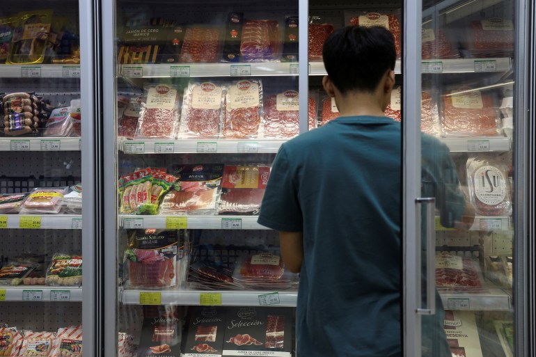 A staff member stocks a freezer where pork and other meat products are displayed