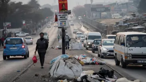 Reuters A woman walks past piles of uncollected trash in the township of Alexandra a day before the national election in Johannesburg, South Africa May 28, 2024