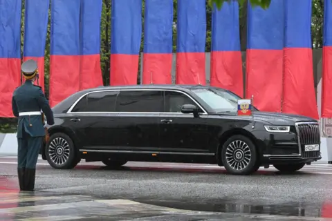 Getty An Aurus Senat car drives in front of flags and behind a figure in military uniform