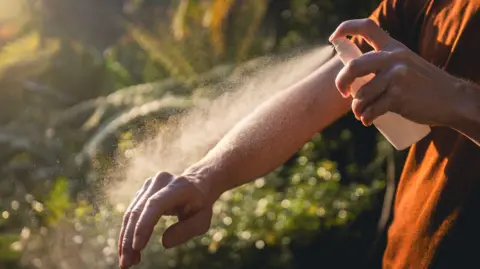 Getty Images Person spraying mosquito repellent on their skin