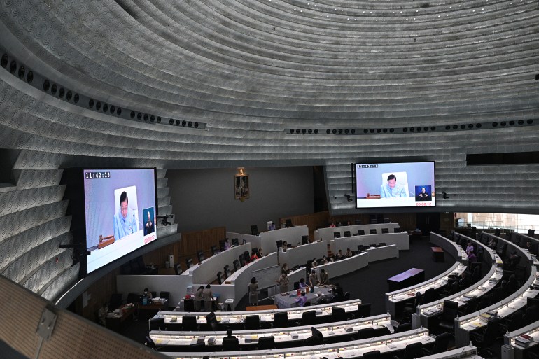 The interior of the Thai Senate in session. It is grey. Seats are arranged in a semi circle with two giant screens at the front on either side.