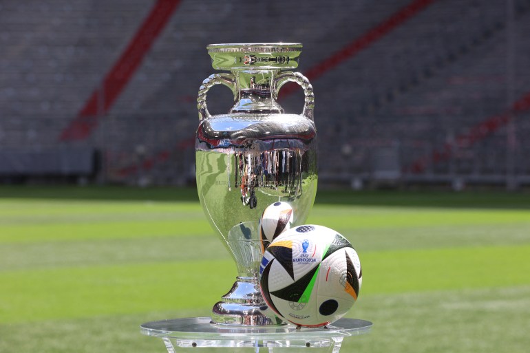 Euro 2024 trophy and ball placed on stadium ground.