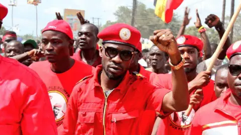 Bobi Wine/Twitter Bobi Wine wearing red overalls at a march with NUP supporters behind him