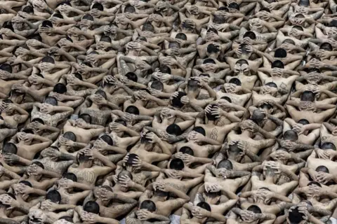 Presidencia El Salvador via Getty Images Prisoners with their hands over their heads and their faces turned away as they are transferred to the mega-jail Cecot in El Salvador