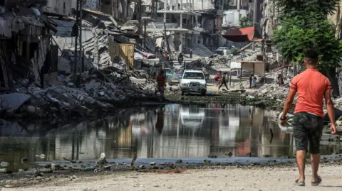 Anadolou via Getty Images A Palestinian man walks towards a pool of water in Gaza