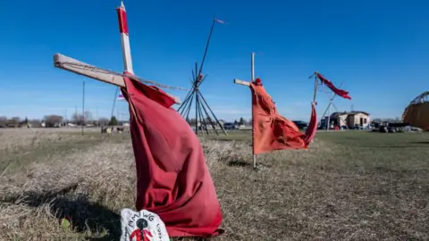 AFP via Getty Images Red dresses on crosses are displayed at the entrance of a makeshift camp near near the Prairie Green landfill in Winnipeg, Manitoba