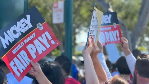 Workers raise signs that read: "Mickey would want fair pay!"