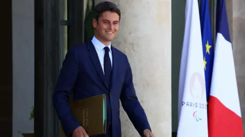 Reuters French Prime Minister Gabriel Attal walking carrying a brown folder