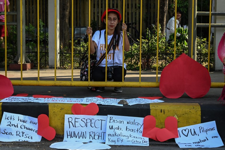 Pro-divorce protesters hold a rally in front of the Senate. One woman is standing behind yellow railings and holding onto them. The protesters have placed red hearts and placards around, One says human rights while another calls for second chances.