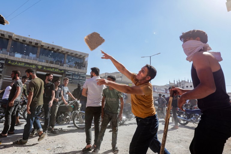 A protester throws a rock towards a Turkish truck during protests against Turkey in al-Bab, in the northern Syrian opposition held region of Aleppo on July 1, 2024. - A man was killed after and Turkish forces clashed in Syria's Ankara-controlled northwest, a war monitor said, in demonstrations sparked by violence against Syrians in Turkey a day earlier. (Photo by Bakr ALKASEM / AFP)