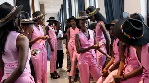 PATRICK MEINHARDT / AFP Contestants in matching pink suits and black hats wait backstage.