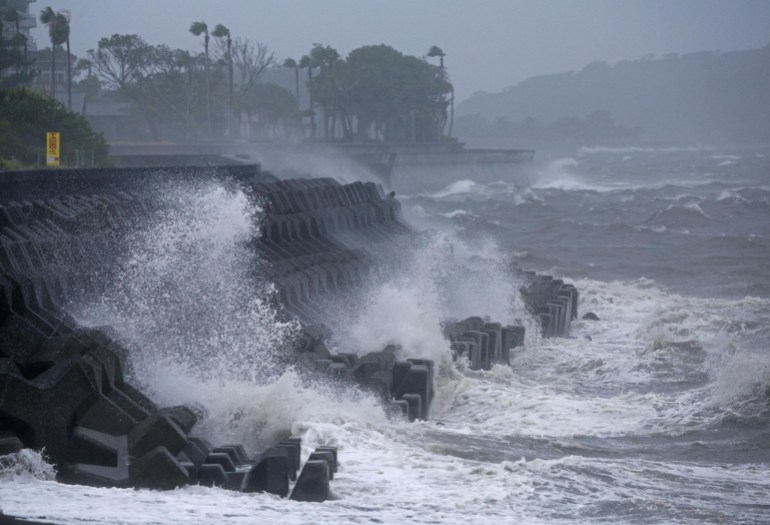 The sea crashing onto cliffs in southern Japan. The tops of the trees are being blown sideways by the wind