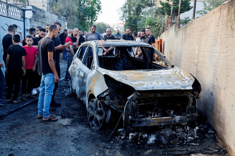 Palestinians assess the damage at the scene of an Israeli strike on a car near Jenin in the Israeli-occupied West Bank