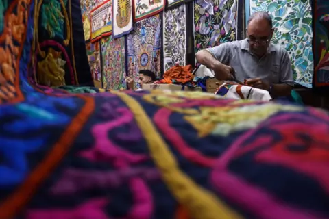 DOAA ADEL / GETTY IMAGES A man sits surrounded by Khayamiya - a decorative Egyptian textile that dates back to Ancient Egypt. He is working on one of the pieces. 