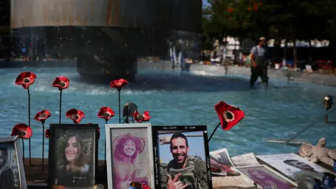 Reuters A man cleans a fountain in Tel Aviv next to photographs of Israelis taken hostage during Hamas's 7 October attacks on Israel (12 August 20240