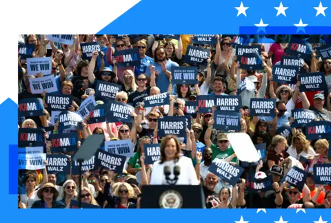 Kamala Harris on stage at a rally with supporters photographed in the background 