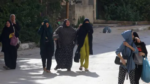 EPA Palestinians, among them women and children, walk past Israeli troops as they leave Jenin refugee camp, 31 August 2024