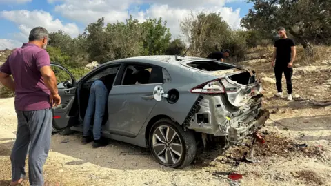 Reuters Palestinians assess damage to a car during a military operation by Israeli forces near Jenin, in the occupied West Bank (28 August 2024)