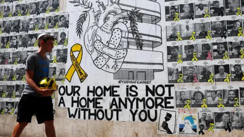 Reuters An Israeli boy walks past a mural in Tel Aviv calling for the return of Israeli hostages held in Gaza, next to posters of the hostages (15 August 2024)