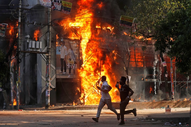 Men run past a shopping center which was set on fire by protesters during a rally against Prime Minister Sheikh Hasina and her government demanding justice for the victims killed in the recent countrywide deadly clashes, in Dhaka