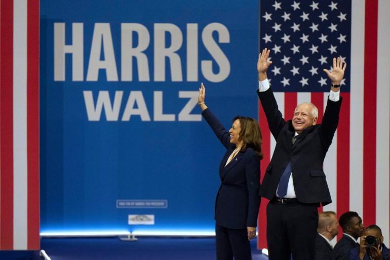 Tim Waltz and Kamala Harris raise their arms on stage in front of their names.