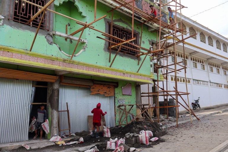 People working on a building. The building is painted green. There is scaffolding around it