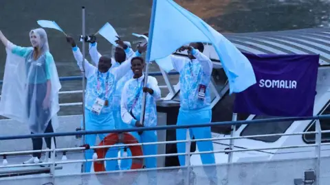 Getty Images Ali Idow Hassan waves a flag on a boat with members of Somalia's Olympic delegation