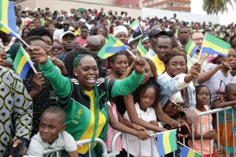 WILFRIED MBINAH / AFP Residents wave flags during a military parade for Gabon Independence Day.