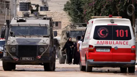 EPA An Israeli military vehicle stops beside a Palestinian Red Crescent ambulance in Jenin, in the occupied West Bank (28 August 2024)