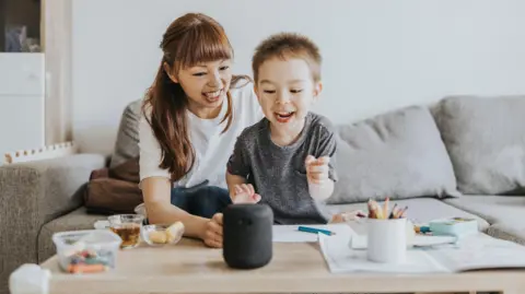 Getty Images A young mother and her young son speak to a smart speaker on the table in front of them