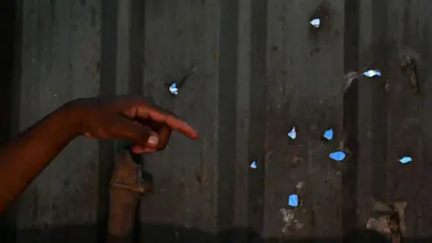 Getty Images The hand of a Masungi Georeserve ranger is seen pointing at bullet holes on on a metal wall