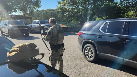 Laurel County Sheriff's Office A man in tactical gear holding a gun surrounded by cars on a highway.