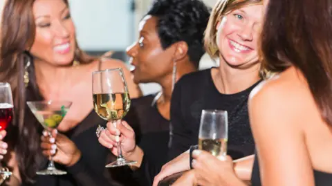 Getty Images Four women in their thirties chatting with drinks in their hands