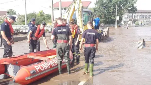 Reuters Firefighters move an inflatable red rescue boat into position on a flooded road in Romania.