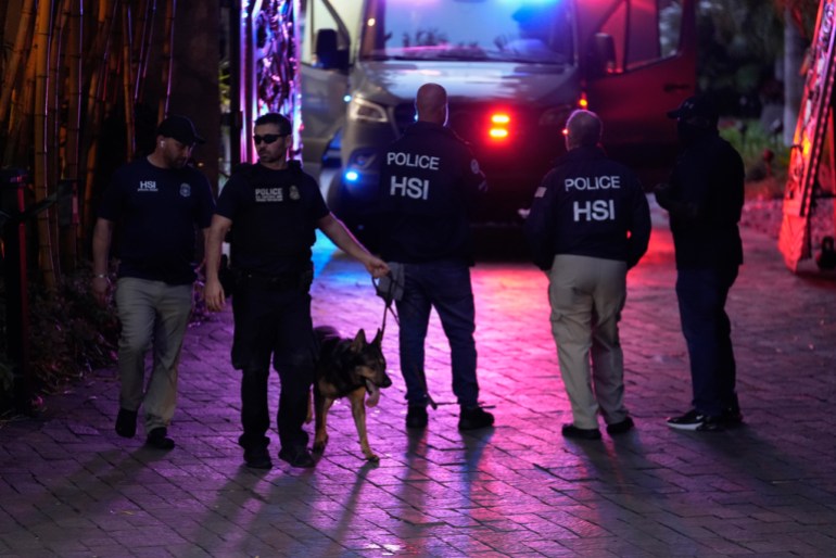 A law enforcement officer leads out a canine as federal agents stand at the entrance to a property belonging to rapper Sean "Diddy" Combs