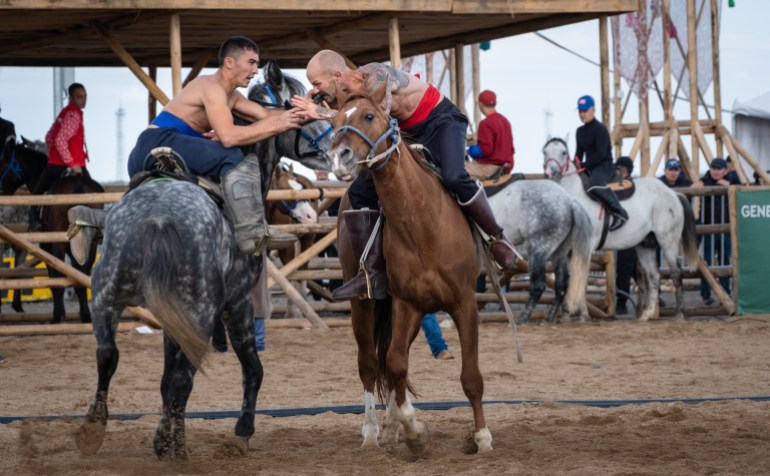 Two men wrestling on horseback