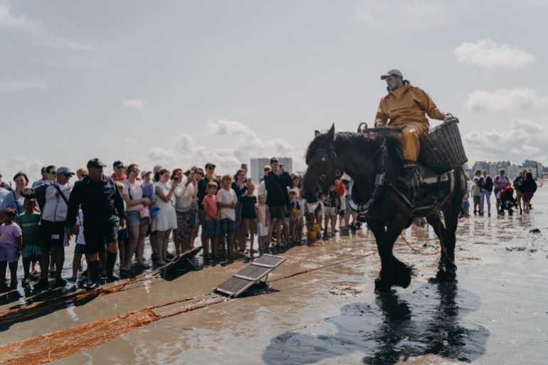 A crowd of visitors watches Gregory Debruyne as he brings the fishing nets out of water in Oostduinkerke, Belgium in July 2024. Photo by Diana Takacsova.