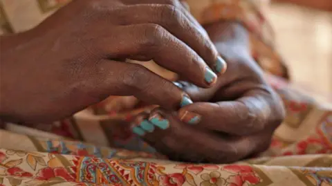 BBC / Hassan Lali Close up of a woman's hands, with chipped blue nail polish.