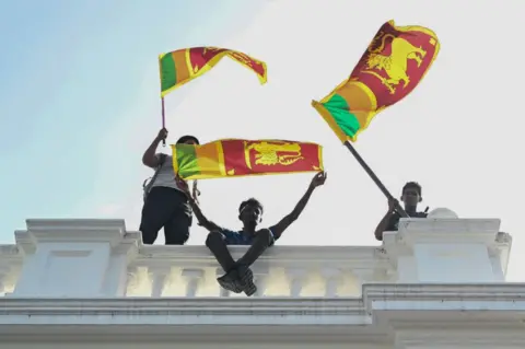 Getty Images Three young men wave Sri Lankan fans from atop a white concrete balustrade