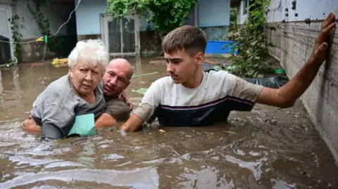 Getty Images Local residents rescue an elderly man (C) from the rising flood waters in the Romanian village of Slobozia Conachi, 14  September 2024. 