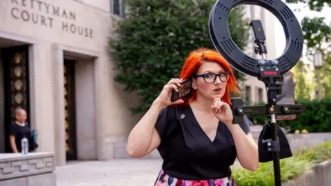 Getty Images Tiffany Cianci shown holding her smartphone to her ear while filming herself on a smartphone attached to a ring light outside a courthouse in Washington, DC.