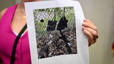 Getty Images Palm Beach County Sheriff PIO Teri Barber holds photographs of the rifle and other items found near where a suspect was discovered during a press conference regarding an apparent assassination attempt of former President Donald Trump on September 15, 2024, in West Palm Beach, Florida.