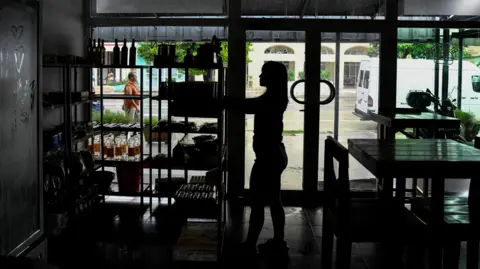 Reuters A woman works in a restaurant during a blackout in Havana, Cuba. She's in shadow and is looking at something on a rack of shelves.