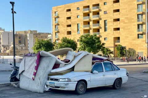 Car with mattresses on top, in front of apartment block