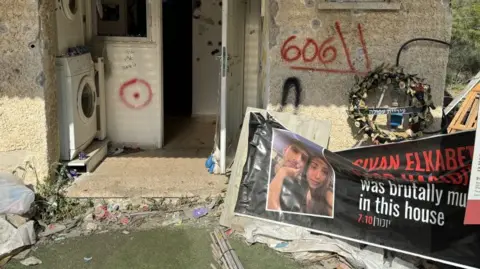 A faded poster displays victims of the Hamas 7 October attack in Kibbutz Kfar Aza outside of their former house